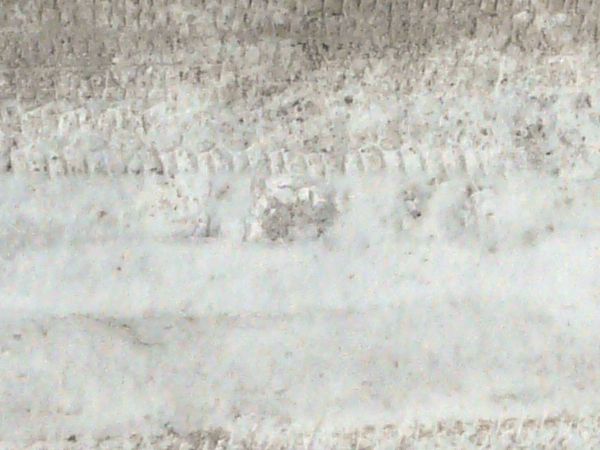 Road texture with thin layer of snow on surface and dark tire marks.